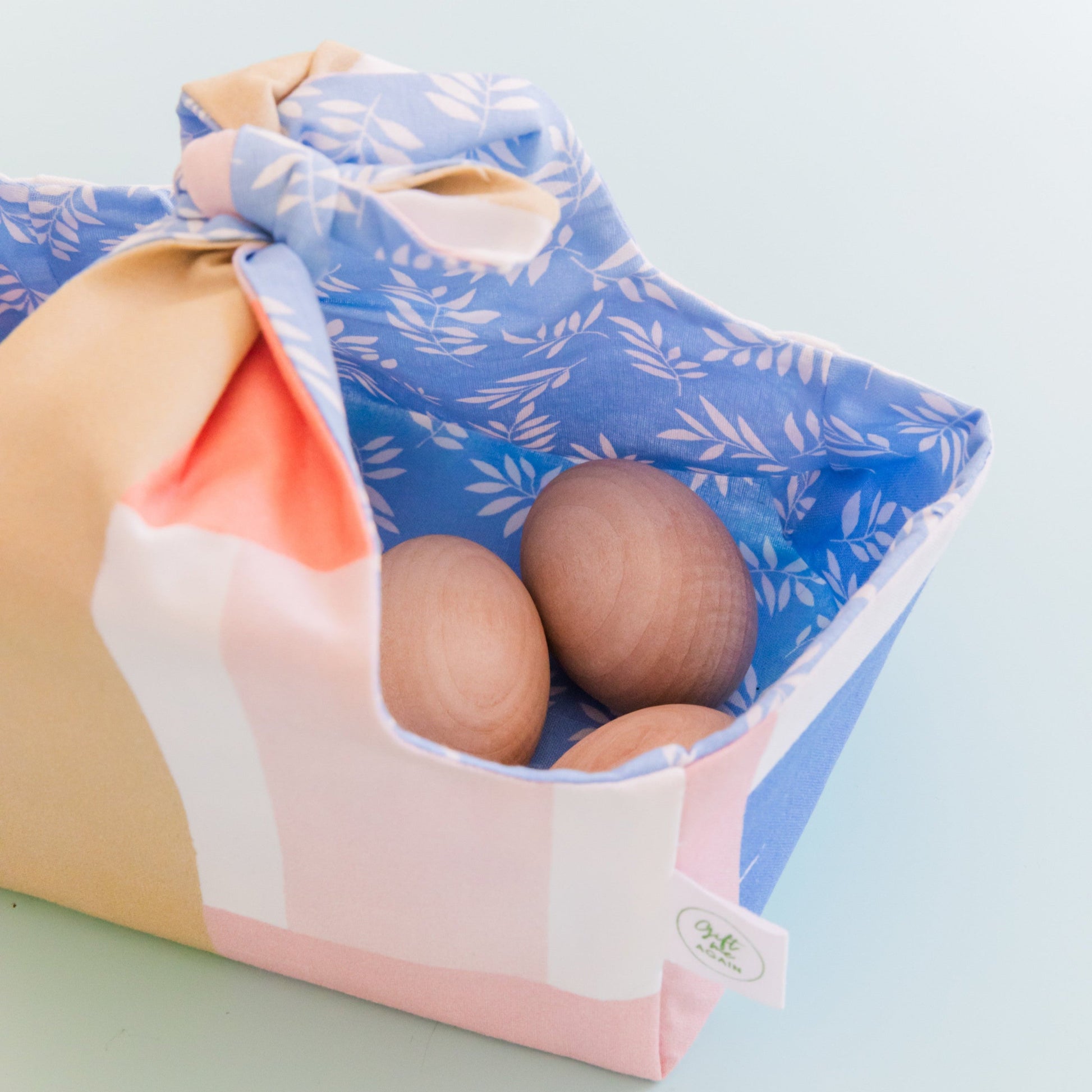 Reusable fabric Easter basket with pastel brushstroke exterior and blue leaf print lining, filled with wooden eggs.