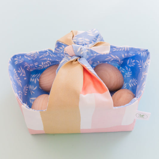 Reusable fabric Easter basket with pastel brushstroke exterior and blue leaf print lining, filled with wooden eggs.