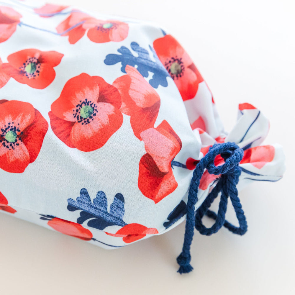 Fabric gift bag in red poppies print against a blue background with a navy cord bow at neck