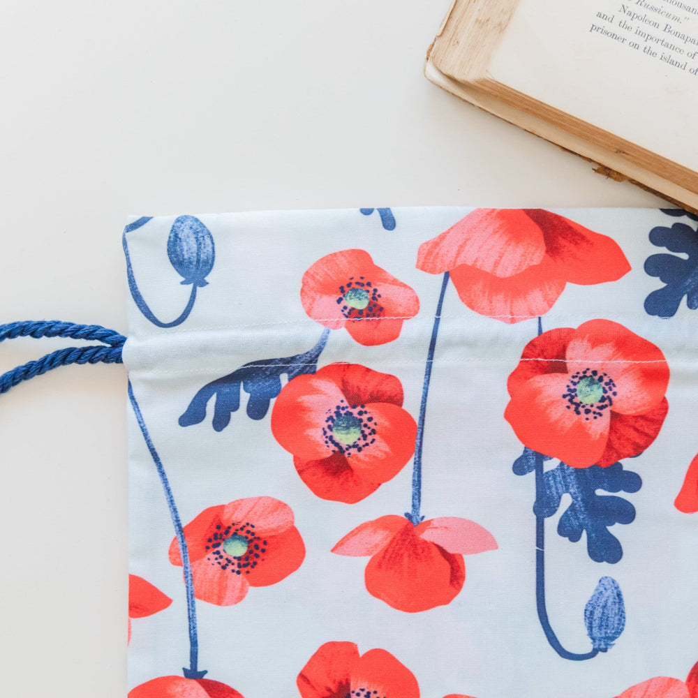 The top of a fabric gift bag featuring red poppies print against blue background with a navy cord