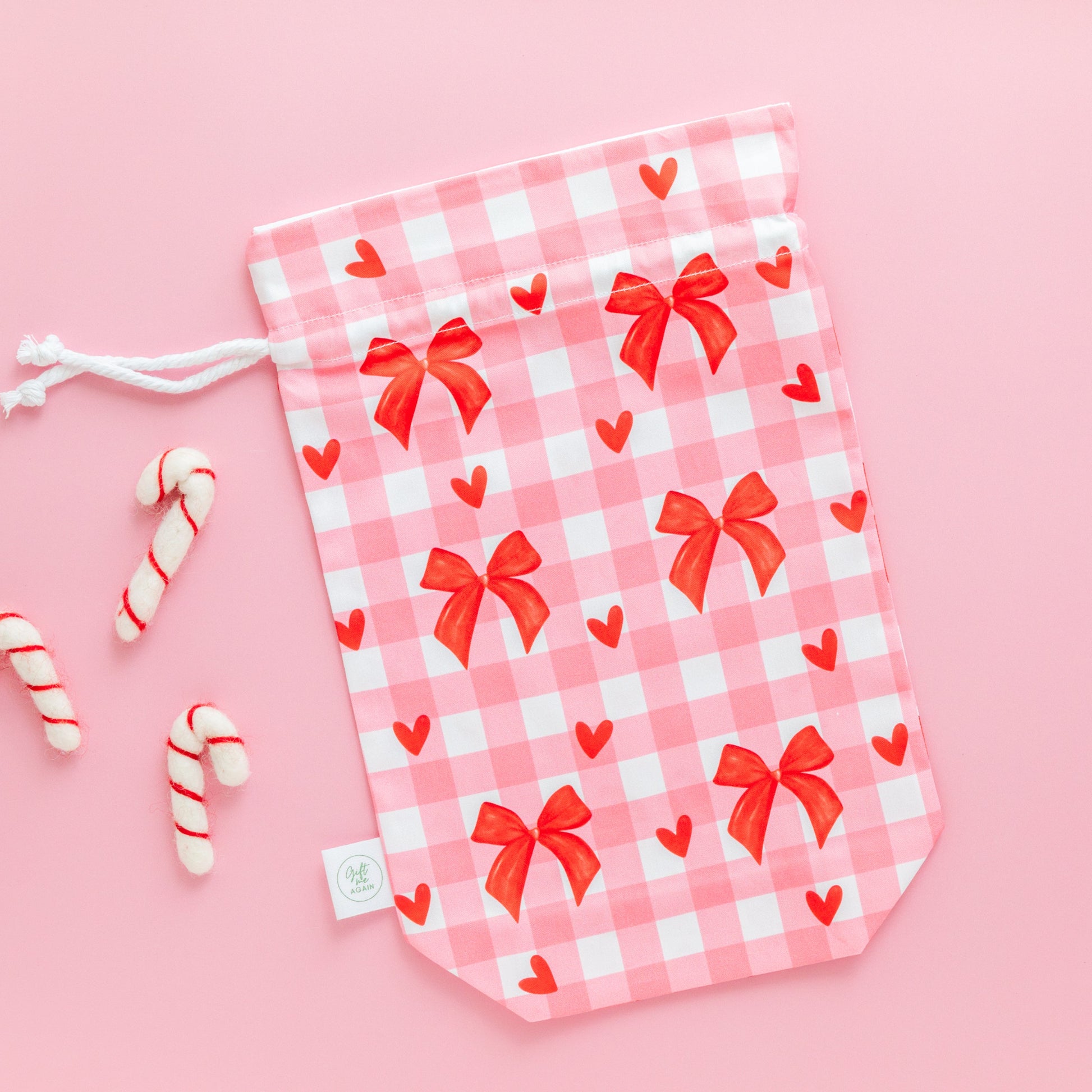 Pink gingham drawstring gift bag with red bows and hearts on a pink background