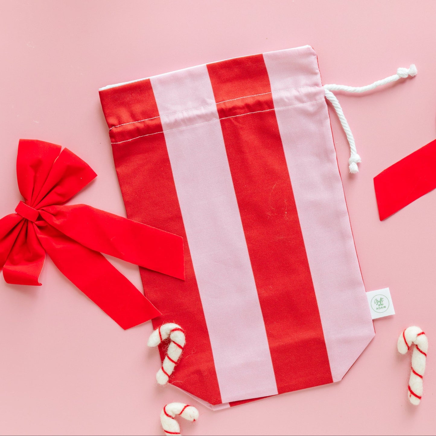 Red and white striped drawstring fabric gift bag with a red bow and candy canes on a pink background