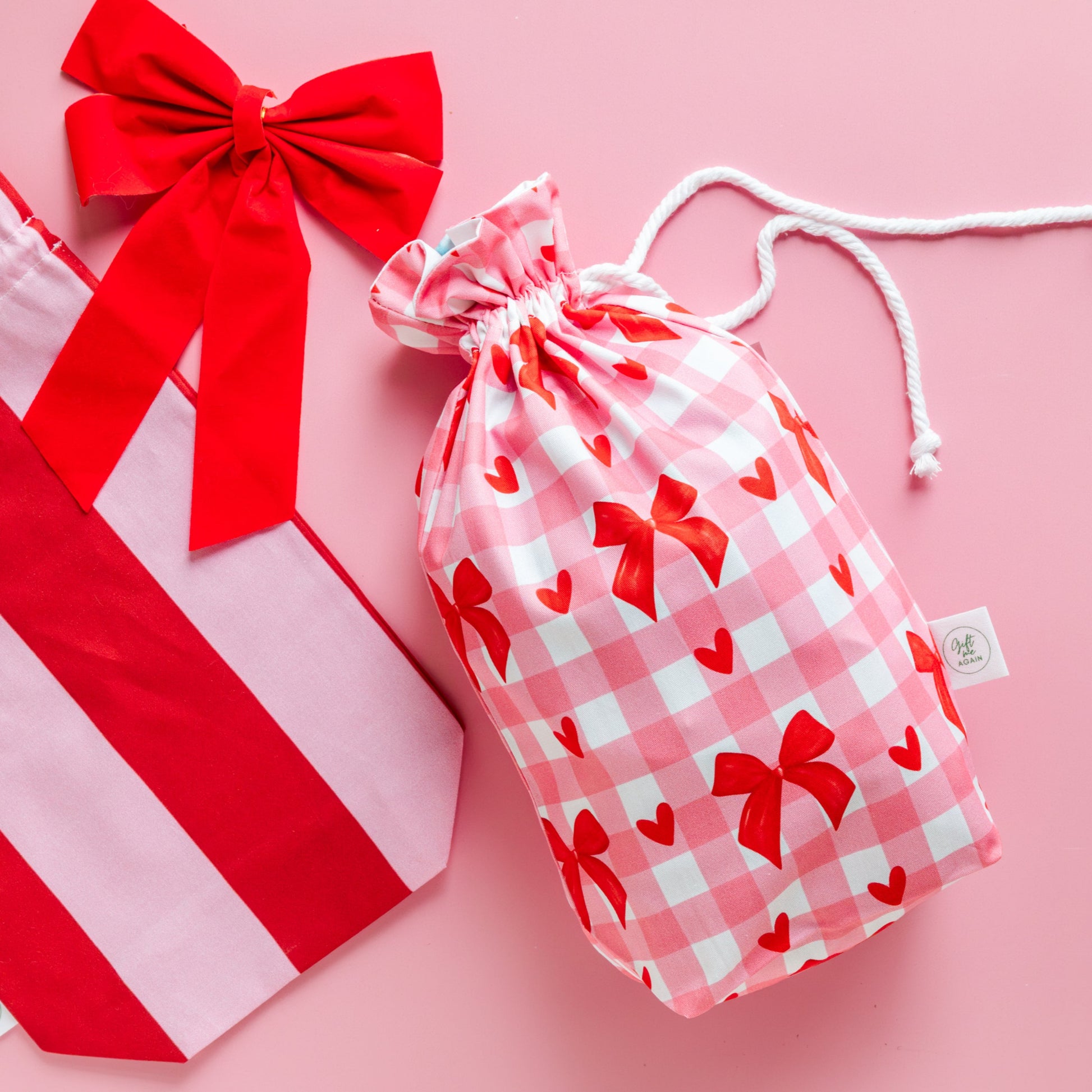 Red and white striped bag with a large red bow and a pink drawstring bag with red bow pattern on a pink background.