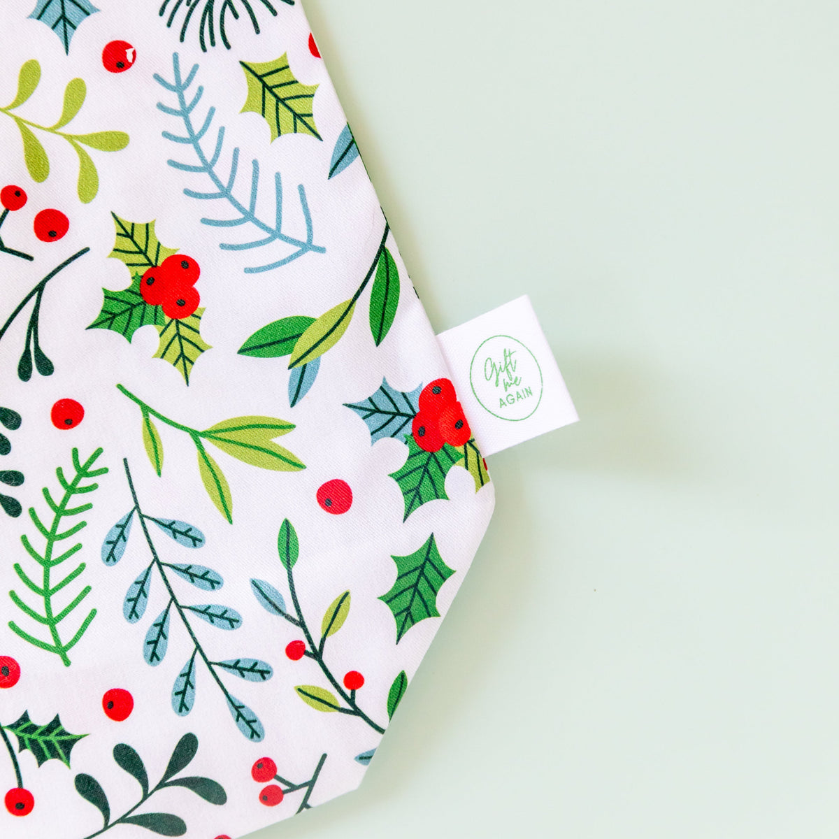 Close-up of Christmas Garden cotton gift bag showing holly, red berries, leafy sprigs and Gift Me Again label.