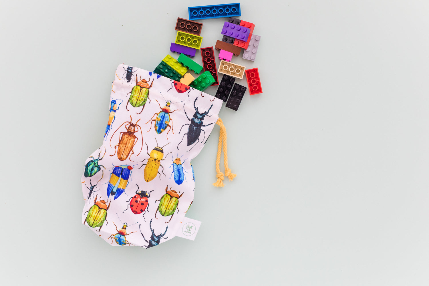 Petite size fabric gift bag in colourful bettle print with yellow drawstring. Lego is spilling from the bag.