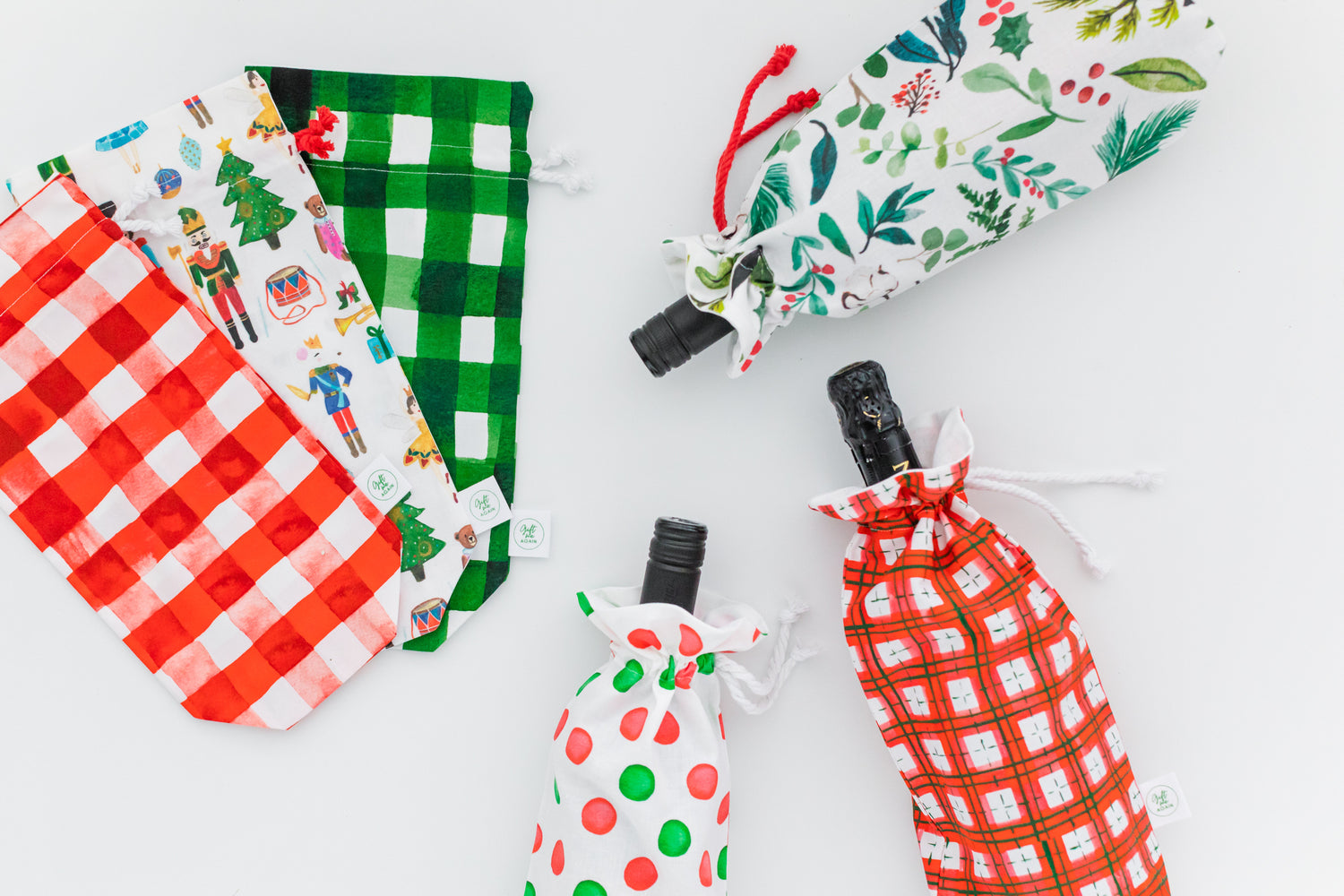 Christmas gift bags in festive prints including red and green gingham, nutcrackers, polka dots, and holiday foliage, shown with wine bottles inside and beside the bags.