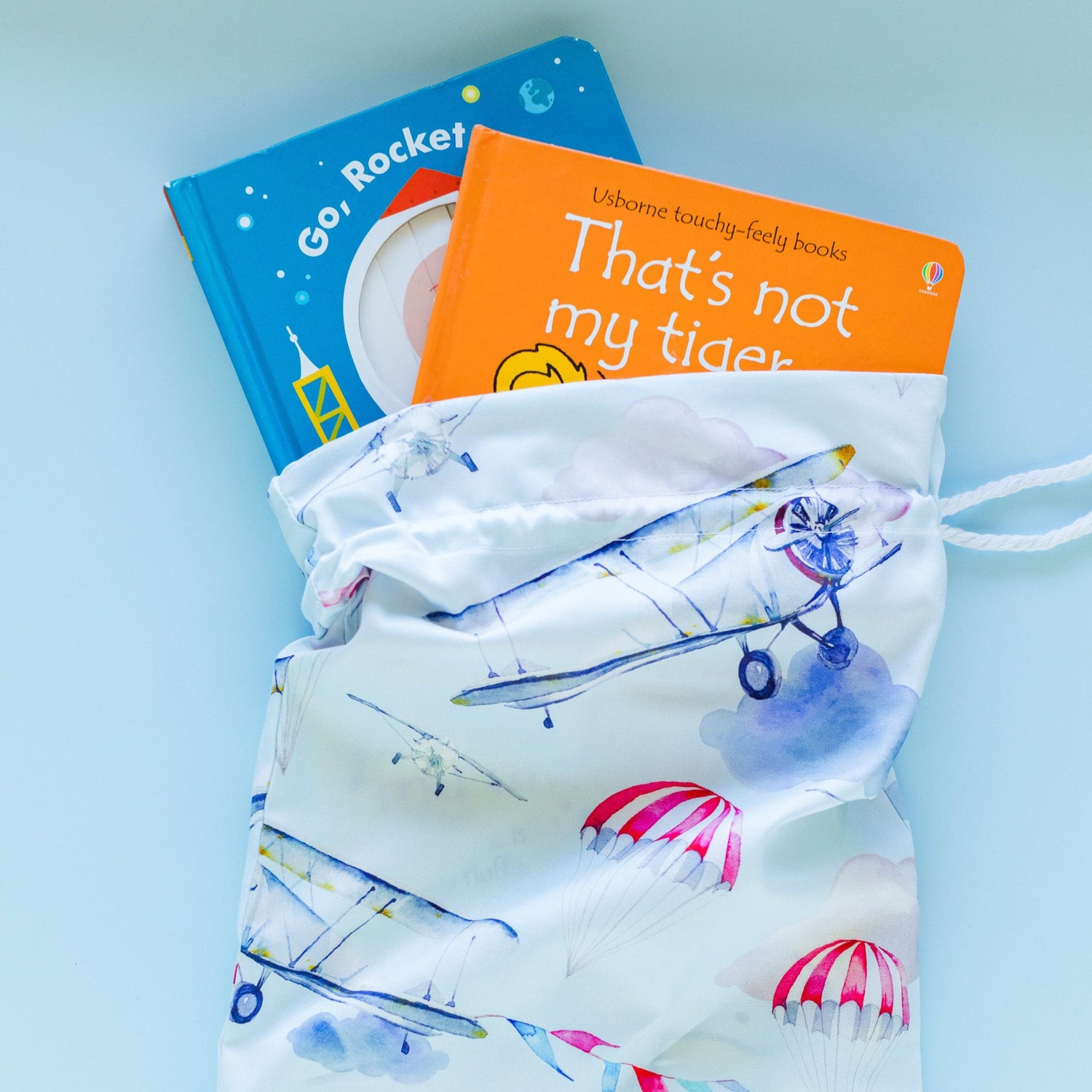A small fabric gift bag in a blue print with aeroplanes and parachutes. There are two children's books in the gift bag.