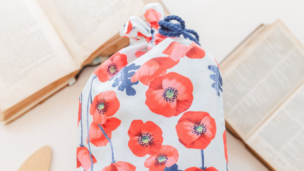 Fabric gift bag in red poppies print against a light blue background