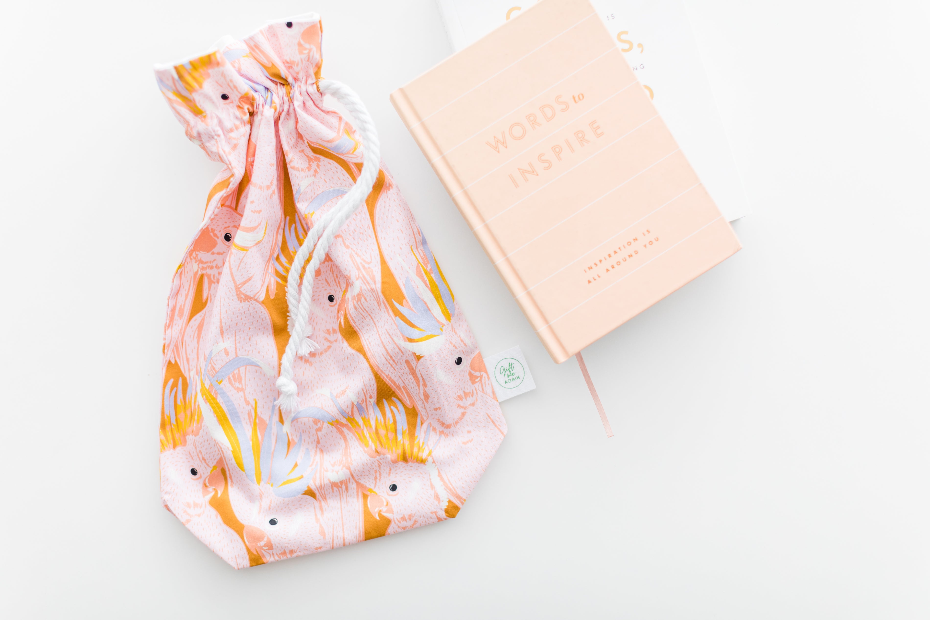 Drawstring bag with pink and orange design next to a pink notebook on a light gray background