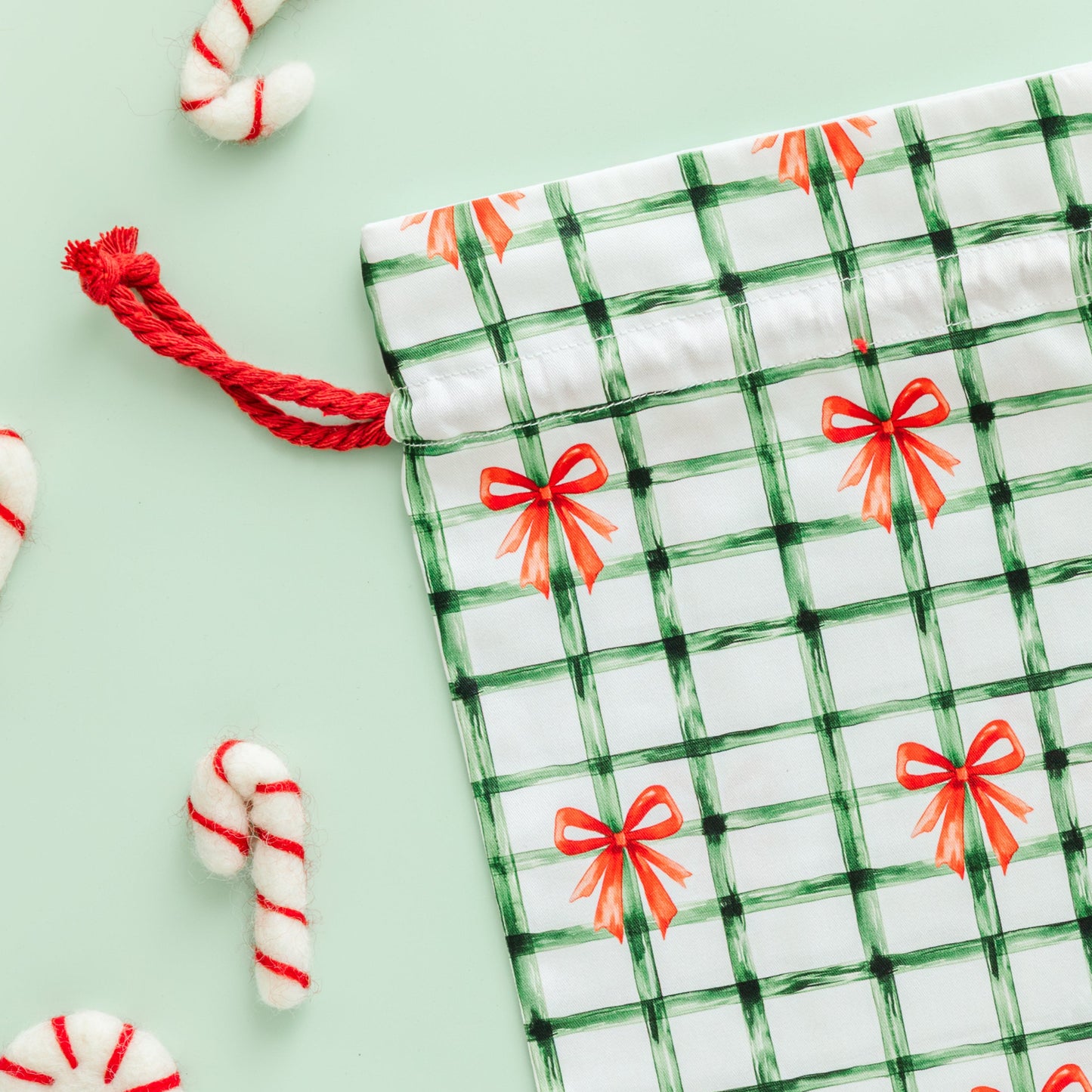 Green and white checkered drawstring gift bag with red bows on a light green background.