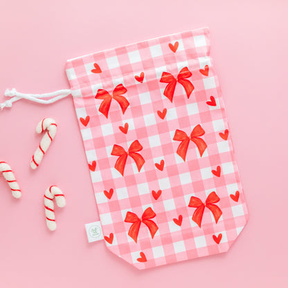 Pink gingham drawstring gift bag with red bows and hearts on a pink background