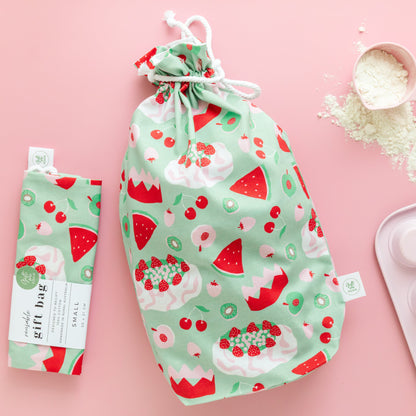 Green reusable gift bag with watermelon, pavlova and fruit pattern on a pink background