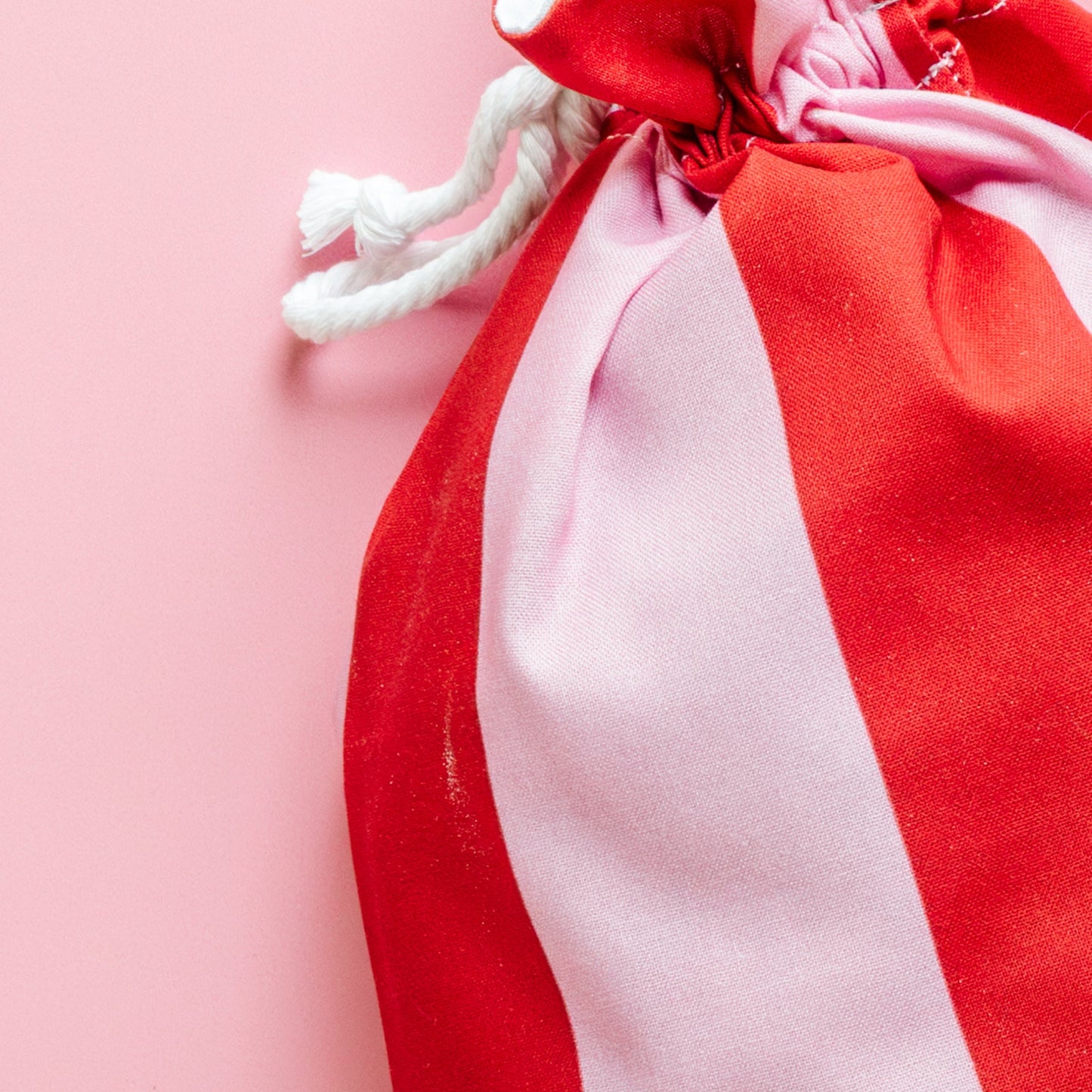 Red and white striped drawstring fabric gift bag on a pink background
