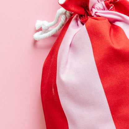 Red and white striped drawstring fabric gift bag on a pink background