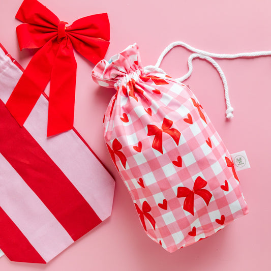 Red and white striped bag with a large red bow and a pink drawstring bag with red bow pattern on a pink background.