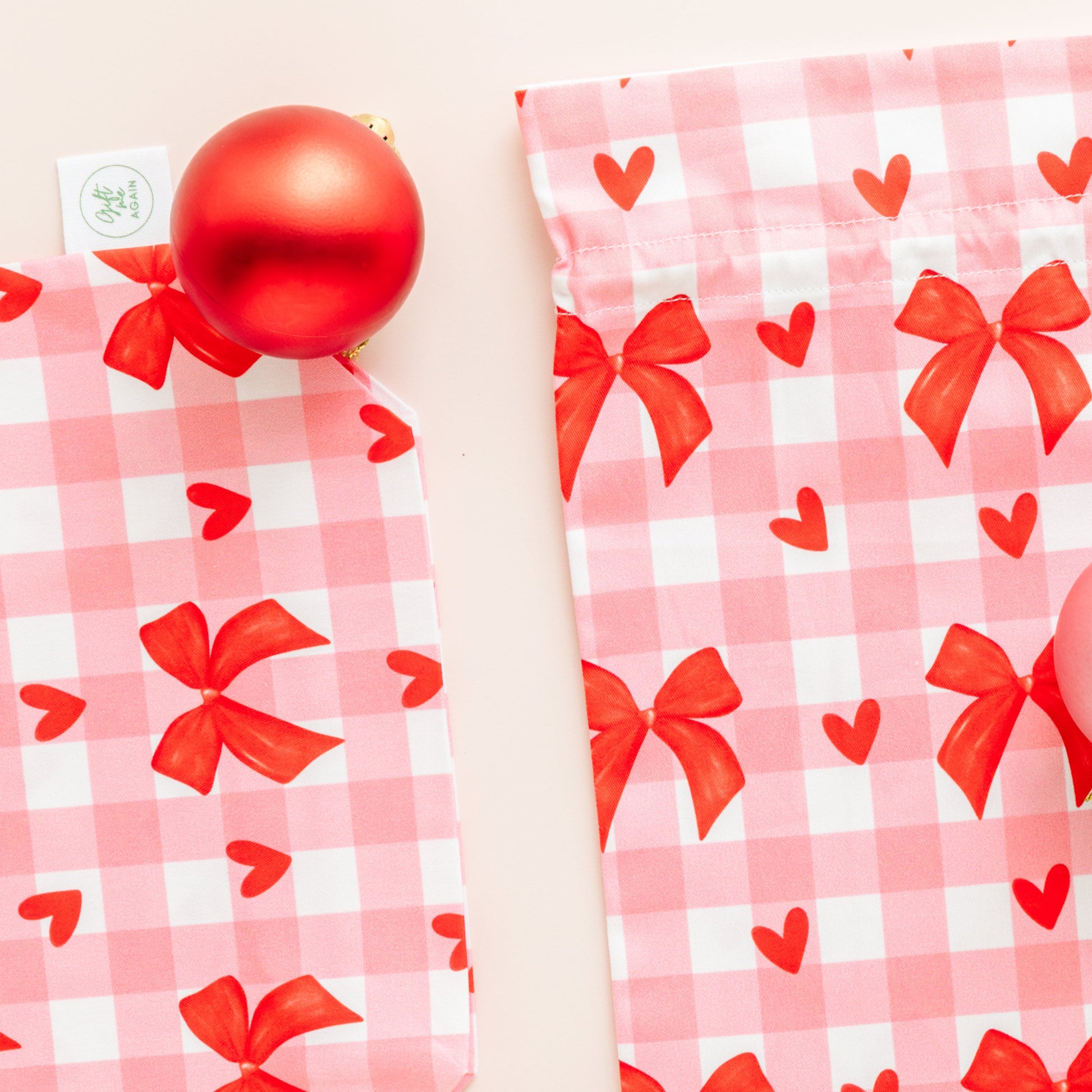 Two pink checkered bags with red bows and hearts on a beige background.