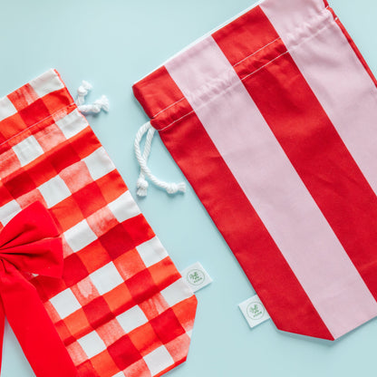 Two fabric gift bags, one red and white checkered with a bow, the other red and white striped, on a light blue background.